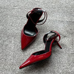 Red high-heeled shoes with thin straps on a gray surface