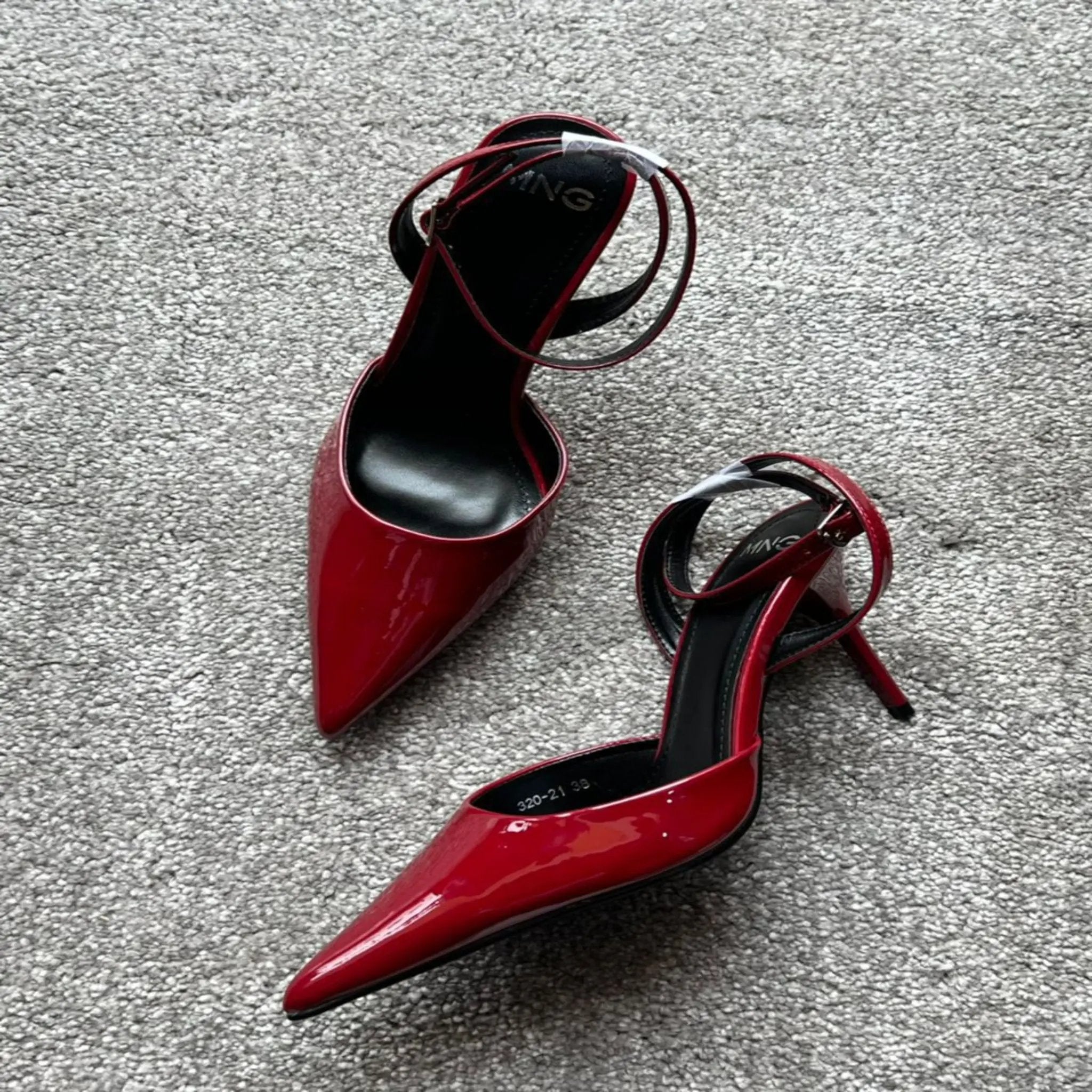 Red high-heeled shoes with thin straps on a gray surface